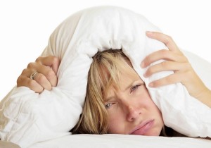 Woman ith her head under her pillow trying to sleep