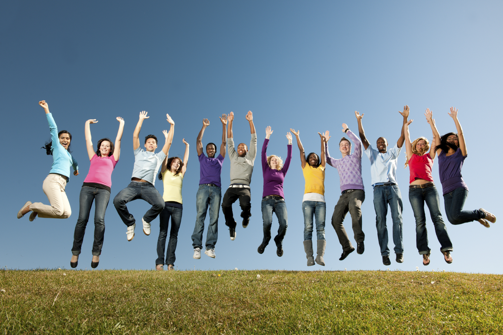 A large group of vibrant young adults outside with a sky backgroun